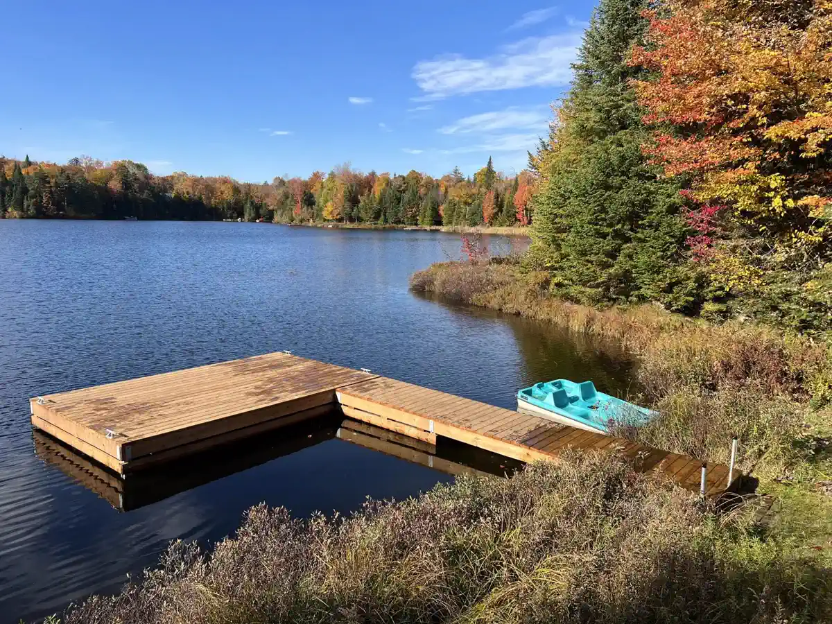 Quai flottant en bois en forme de L installé par Quais Laurentiens sur un lac des Laurentides, à l’automne, avec un pédalo amarré.